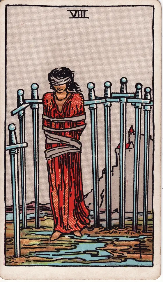 Eight of Swords: A woman, bound and hoodwinked, with the swords of the card about her.