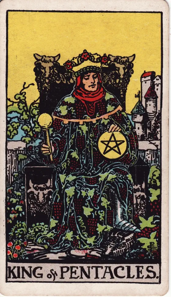 King of Pentacles: A crowned king in a robe covered with grapevines sits on a throne carved with bulls' heads, holding a sceptre and a pentacle, with a castle behind him.