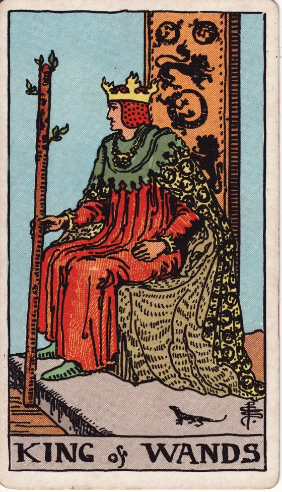 King of Wands: A crowned king in red, seen in profile, sits on a throne hung with lions and salamanders, holding a sprouting wand, with a small salamander on the dais at his feet.
