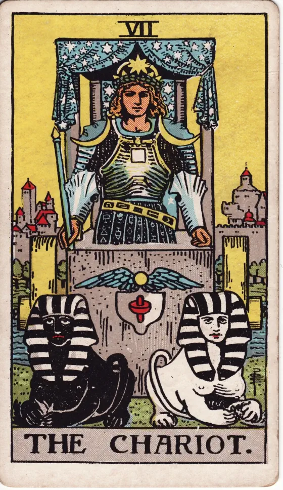 The Chariot: A crowned figure in armour stands in a stone chariot under a starry canopy, holding a wand, with a black sphinx and a white sphinx lying in front and a walled city behind.