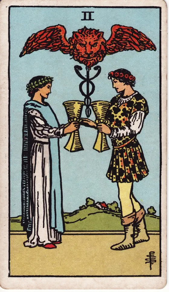Two of Cups: A youth and maiden are pledging one another, and above their cups rises the Caduceus of Hermes, between the great wings of which there appears a lion's head.