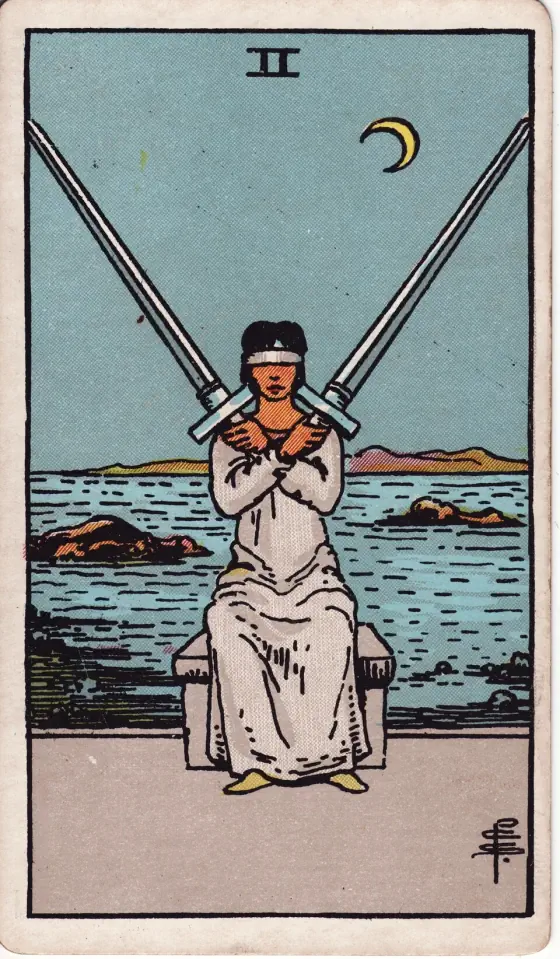 Two of Swords: A hoodwinked female figure balances two swords upon her shoulders.